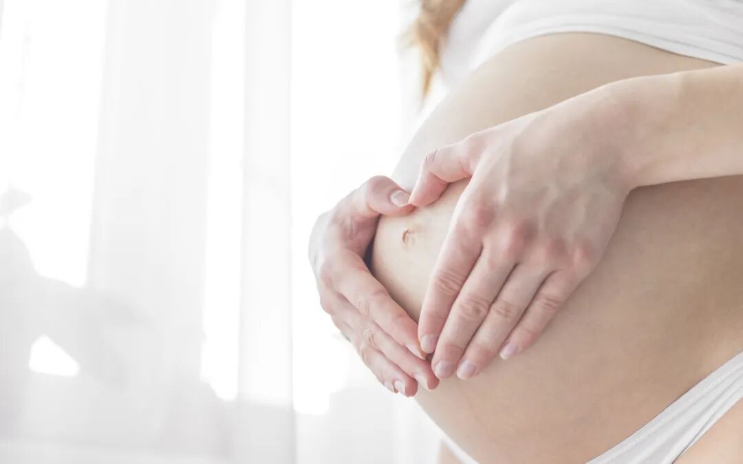 A pregnant woman gently holding her belly during prenatal care at AMCARE Beijing