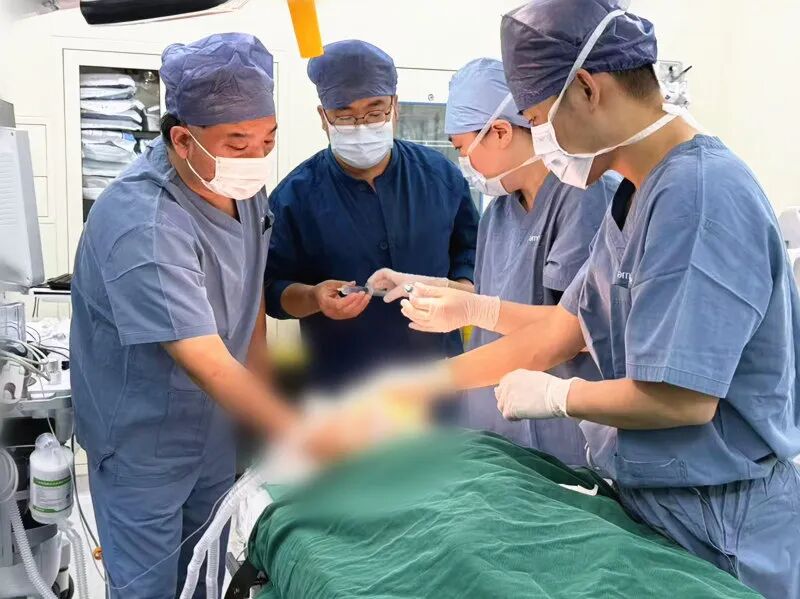 Four clinicians in surgical scrubs working together over a draped patient in an operating theatre