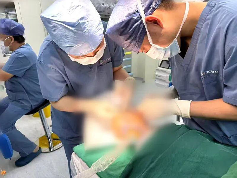 Two surgeons working closely on a draped patient under operating theatre lighting